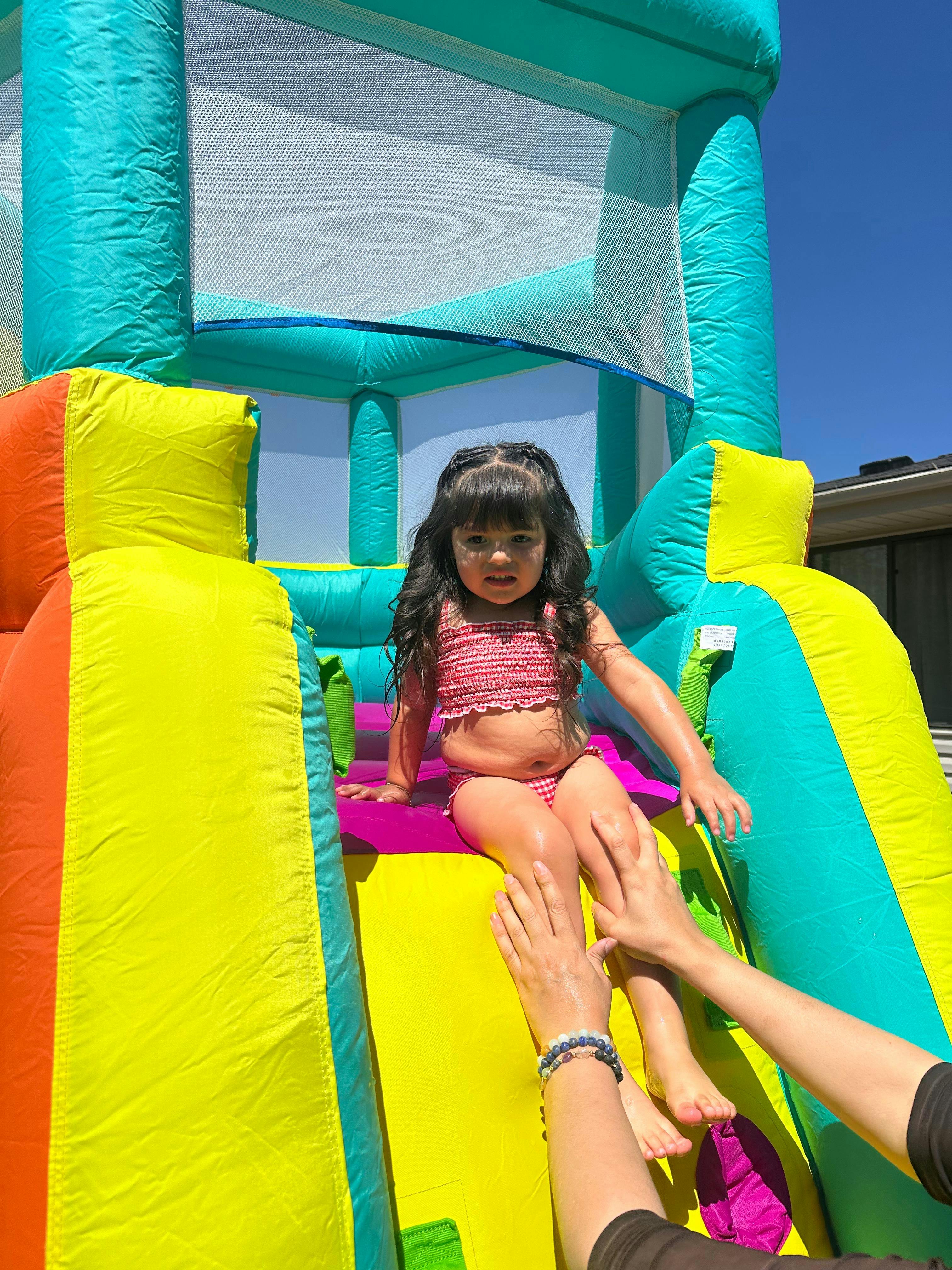 Child in a red and white swimsuit sitting on a colorful inflatable slide