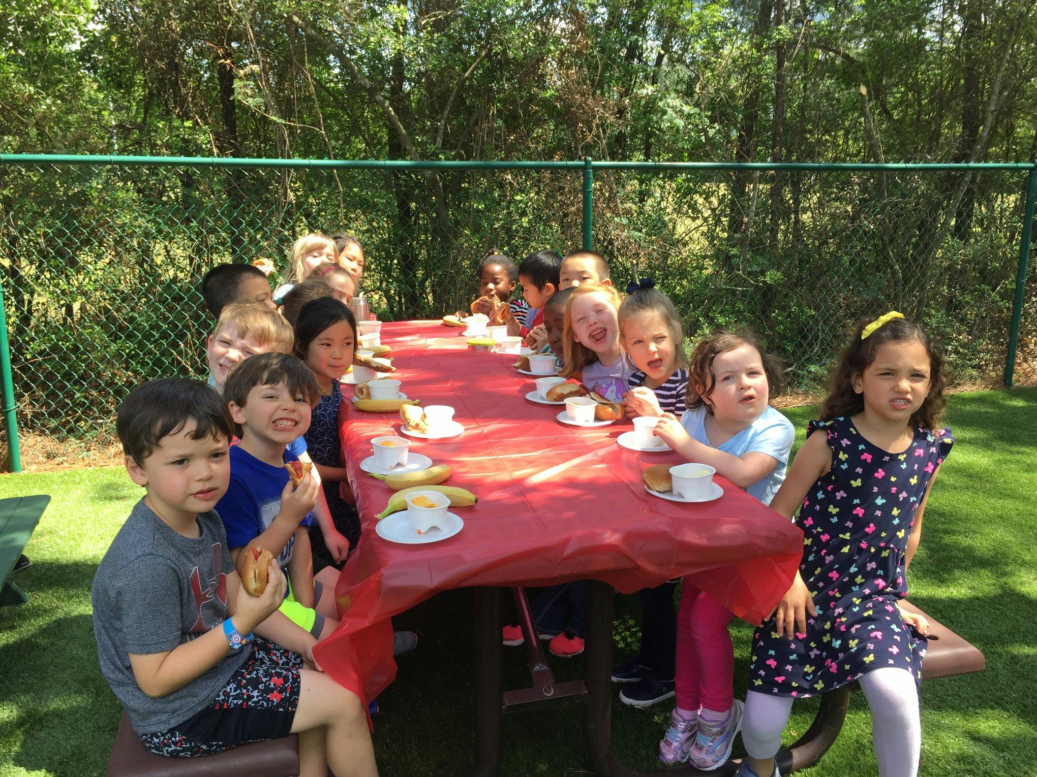 Children sitting at a long table with a red tablecloth and teacups