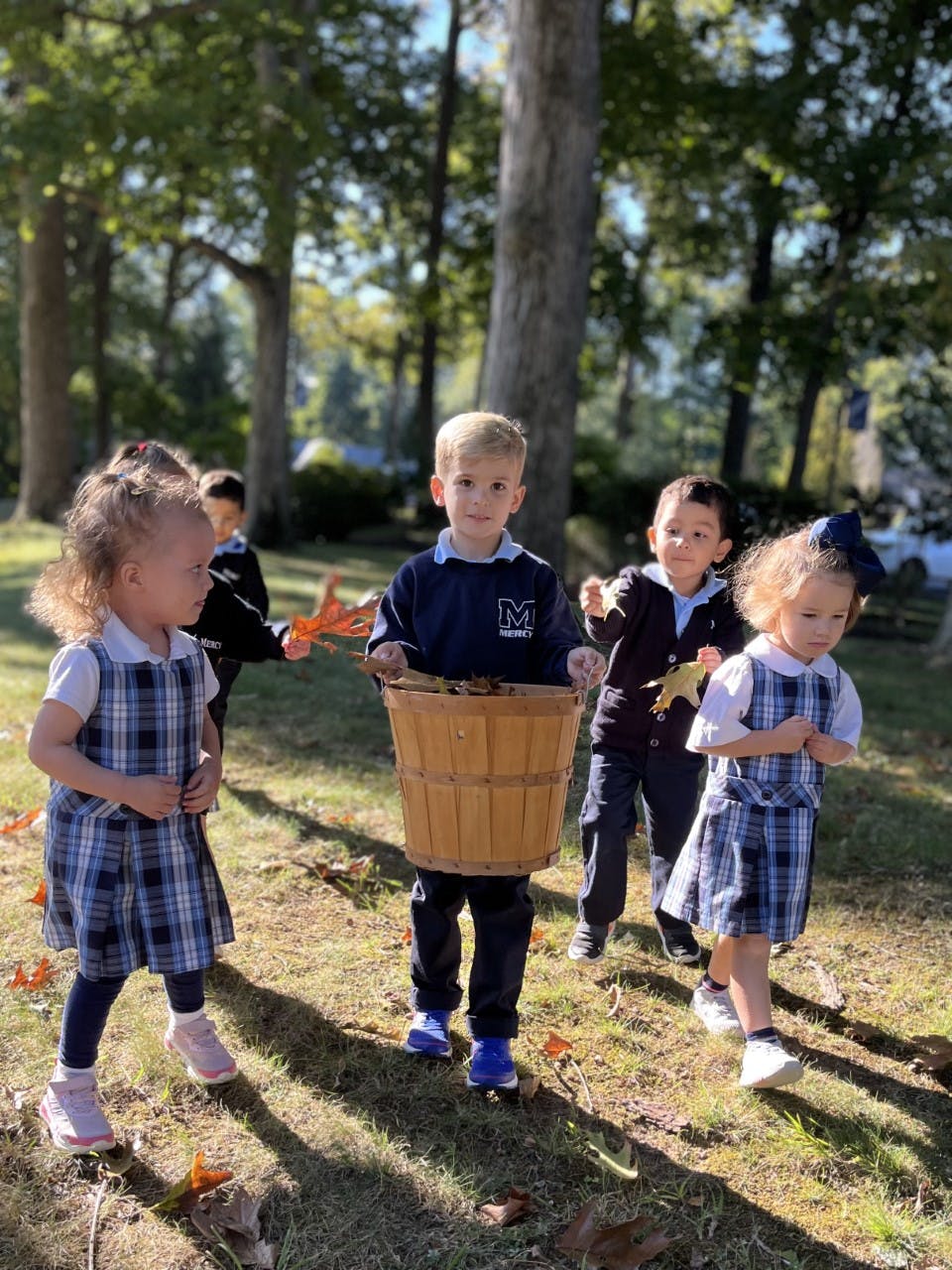 Children in uniform collecting leaves in a basket outdoors
