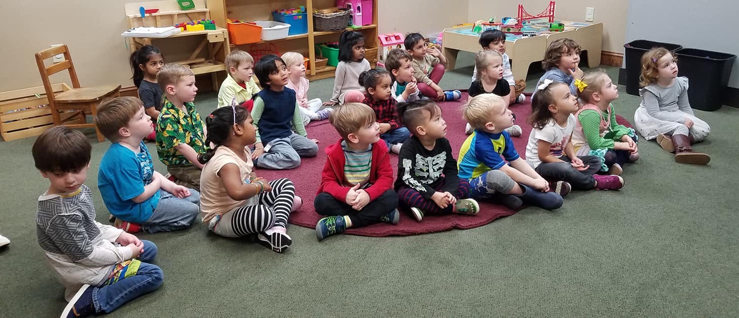 Many children sitting on the floor in a classroom