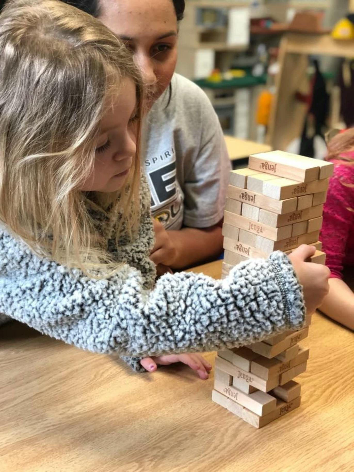 Child playing Jenga with a person watching