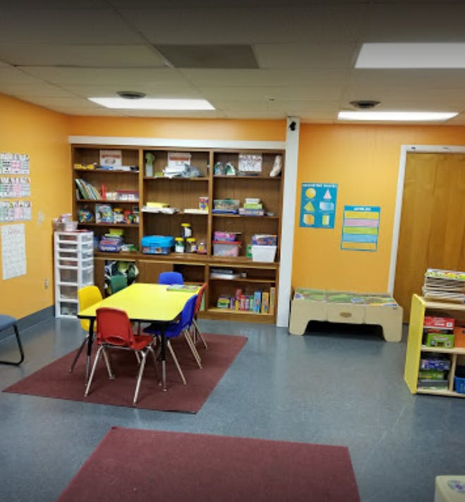 Classroom with a yellow table and colorful chairs, bookshelves, and wall decorations