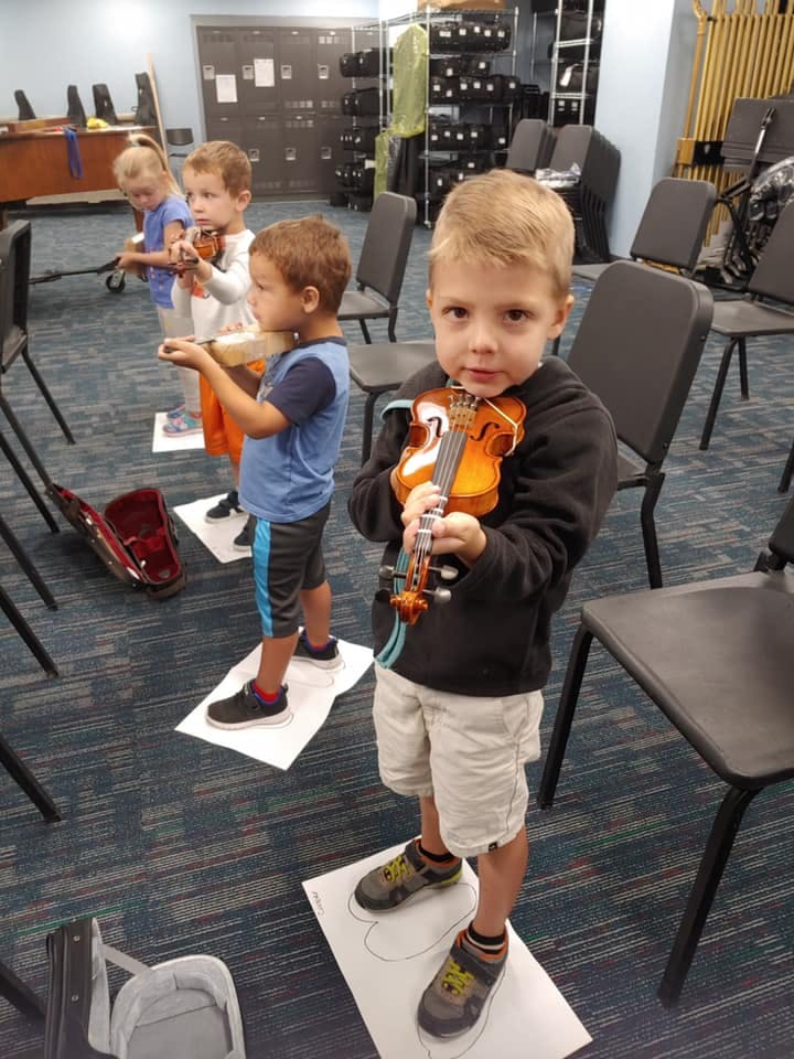 Children learning to play violins in a classroom