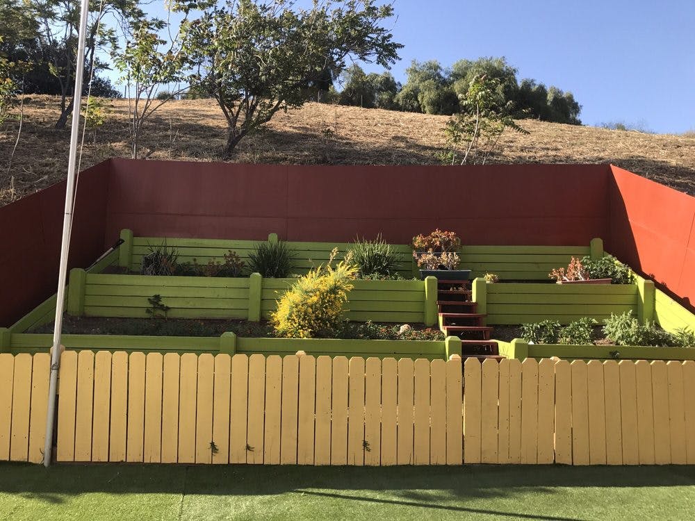 Terraced garden with green planters and a yellow fence