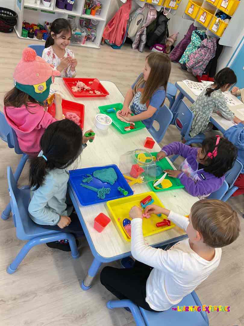 Children playing with clay and toys at tables in a classroom