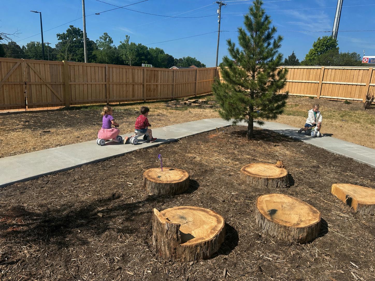 Three children riding small bikes on a paved path outdoors