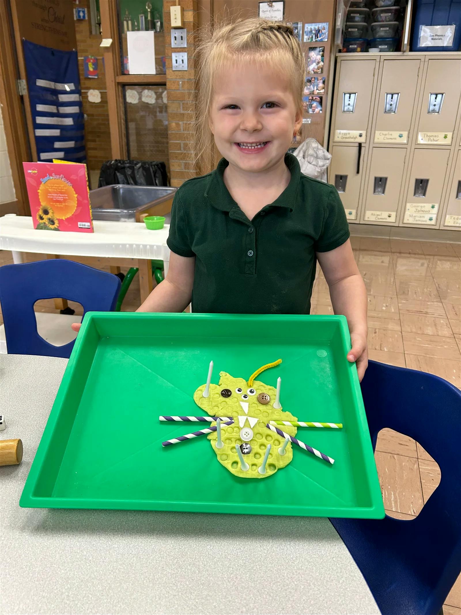 Child holding a green tray with a yellow playdough creation