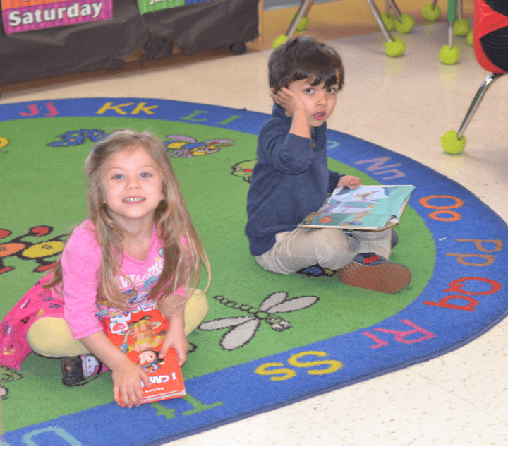 Two children sitting on a rug with books