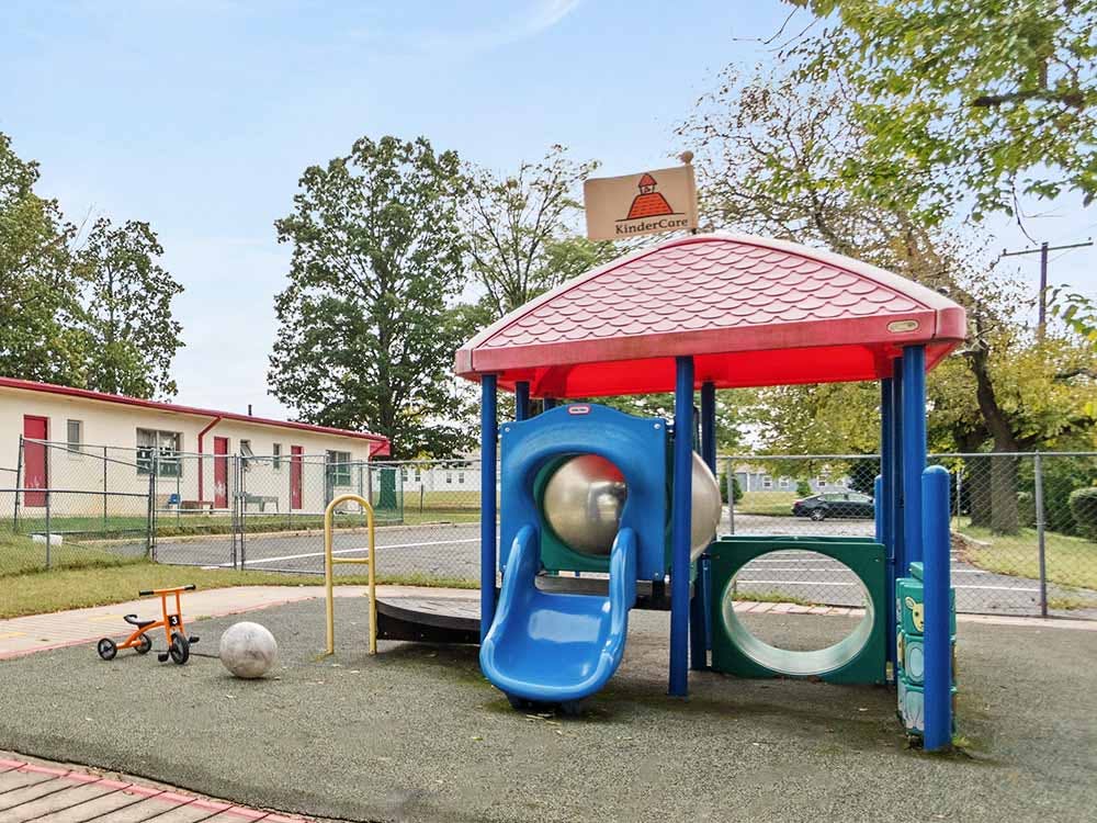 A playground with a slide and climbing structure, buildings in the background