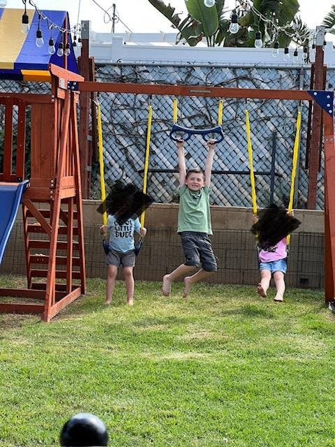 Child hanging from a swing set bar, two other children on swings
