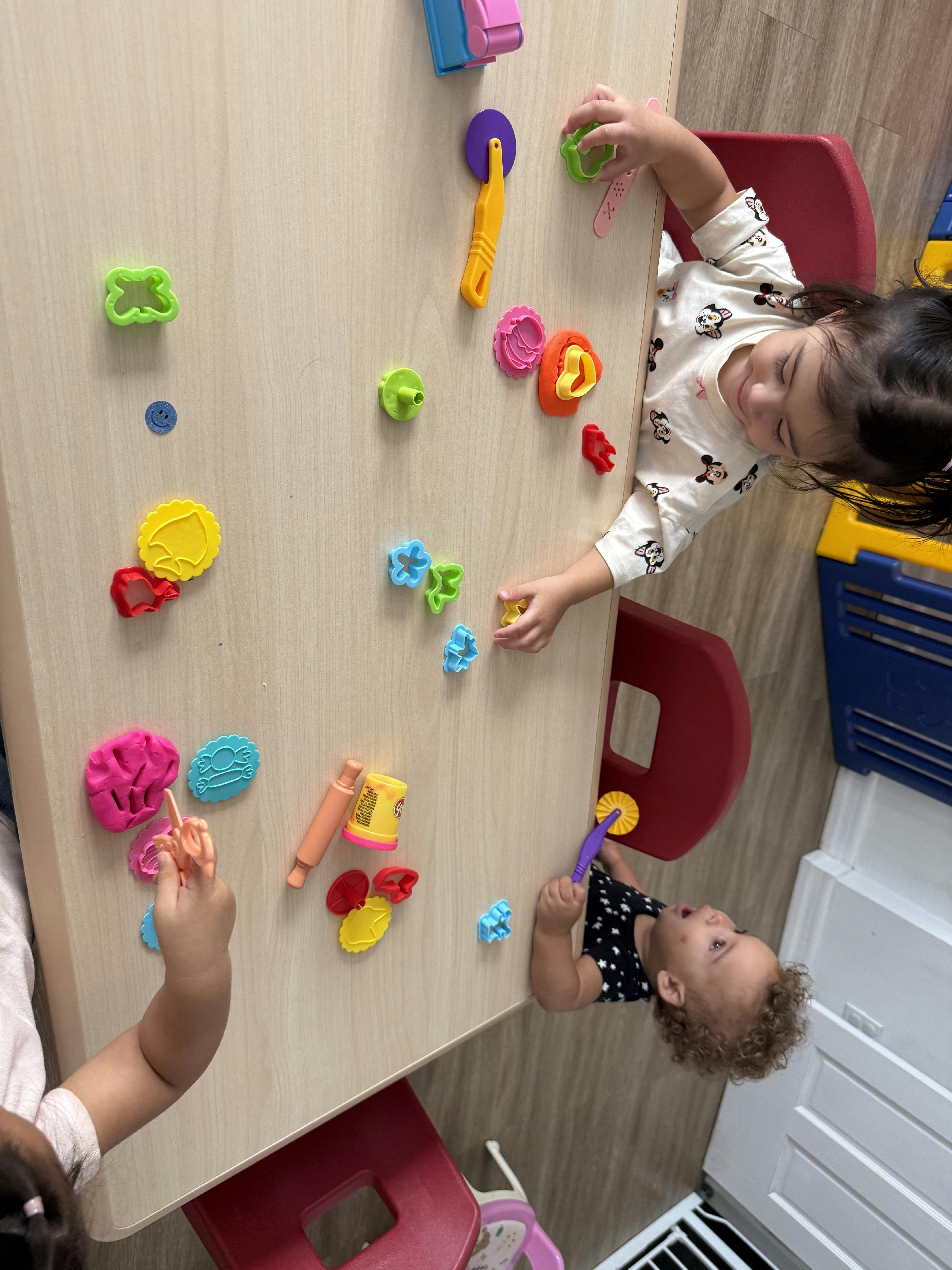 Two children playing with colorful playdough and tools at a table