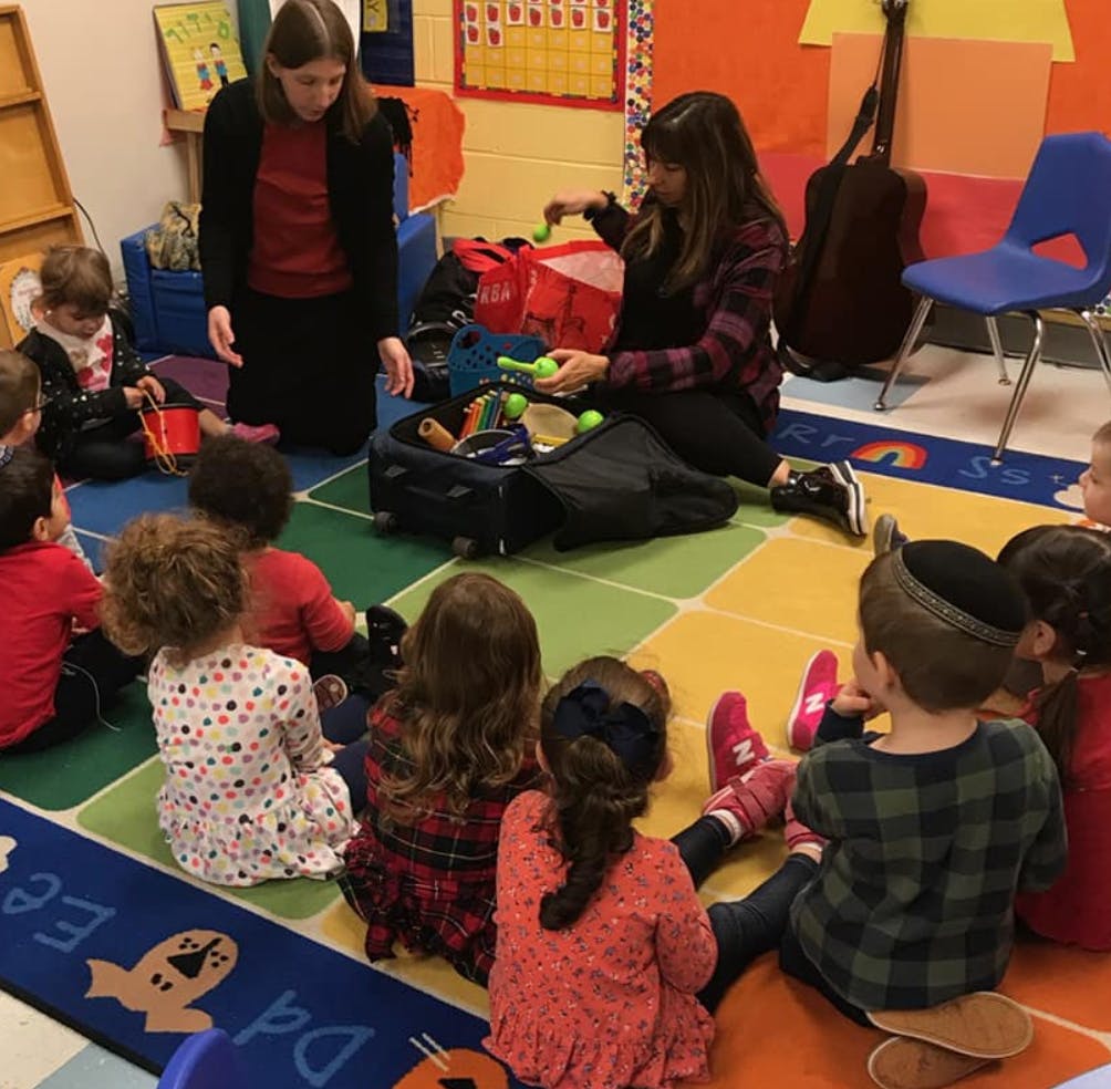 Two people interacting with children sitting on a colorful rug in a classroom