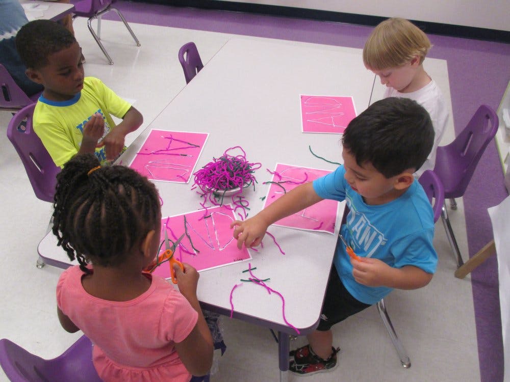 Children at a table doing crafts with pink paper and purple yarn