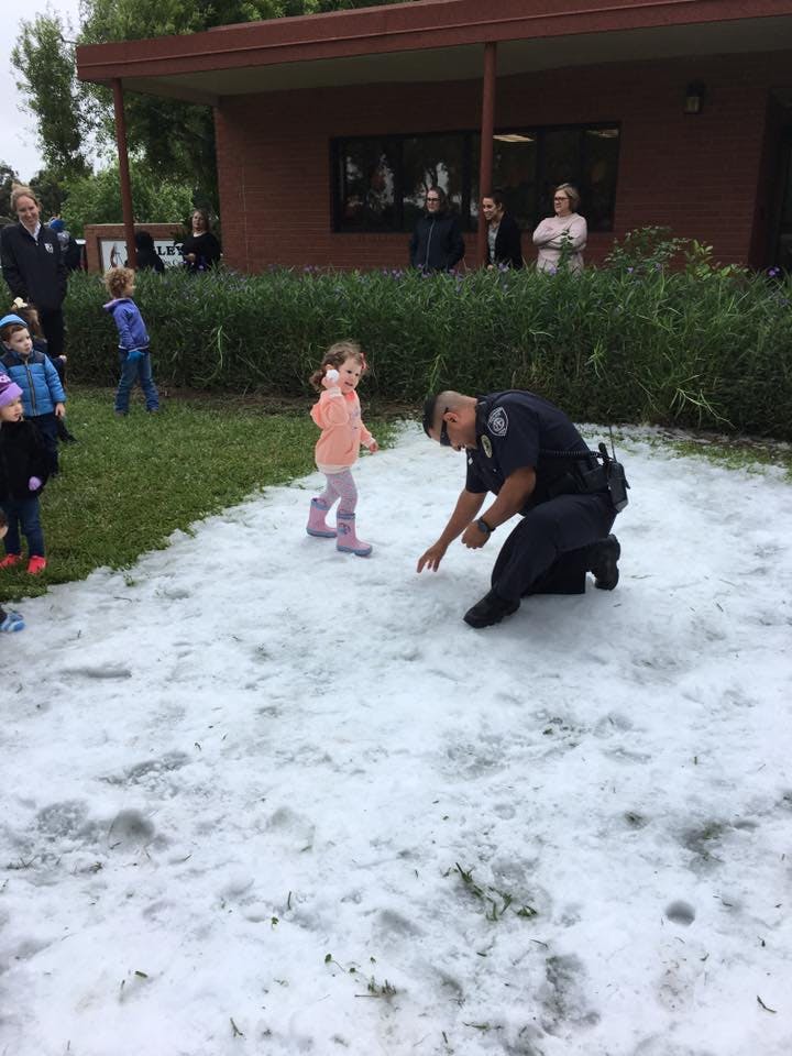 Police officer kneeling in snow with a child standing nearby