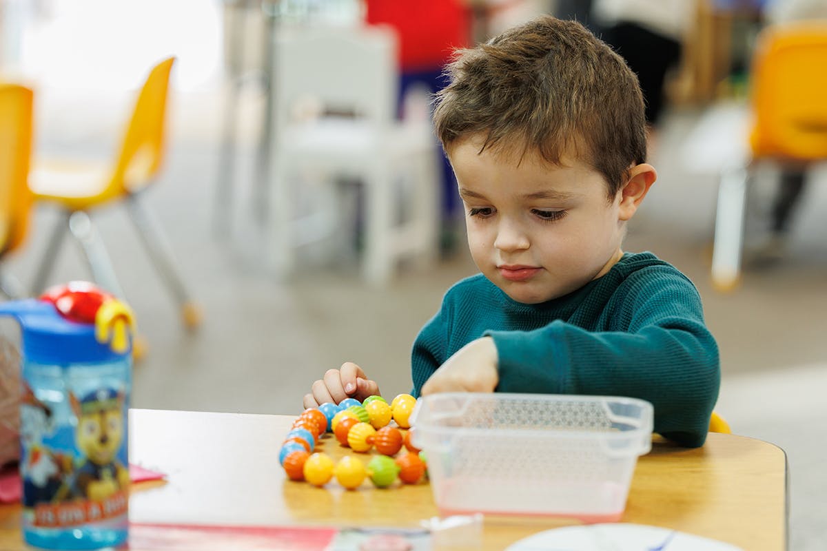 Child playing with colorful beads at a table