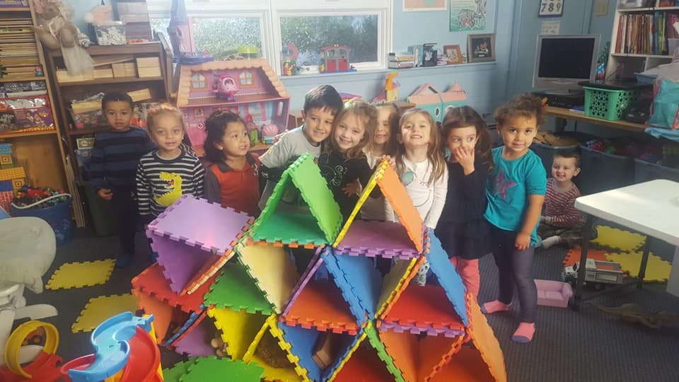 Children standing around a colorful foam block structure in a classroom