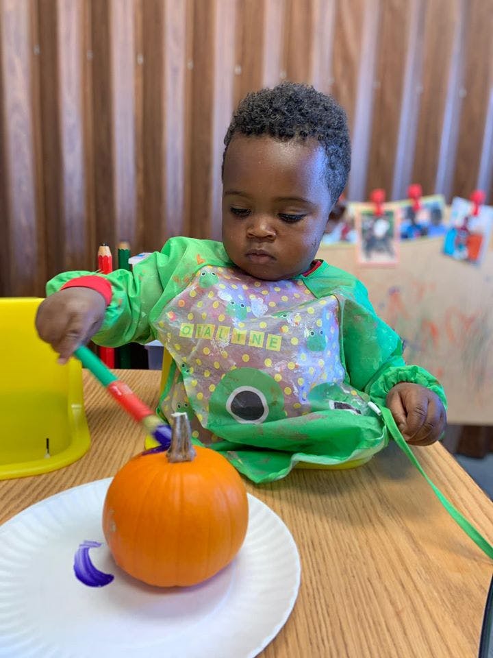 Child in a green smock painting a small pumpkin