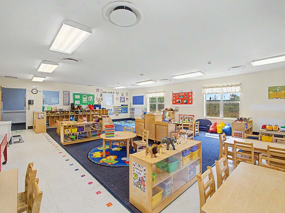 A classroom with small tables, chairs, colorful rugs, and shelves with toys