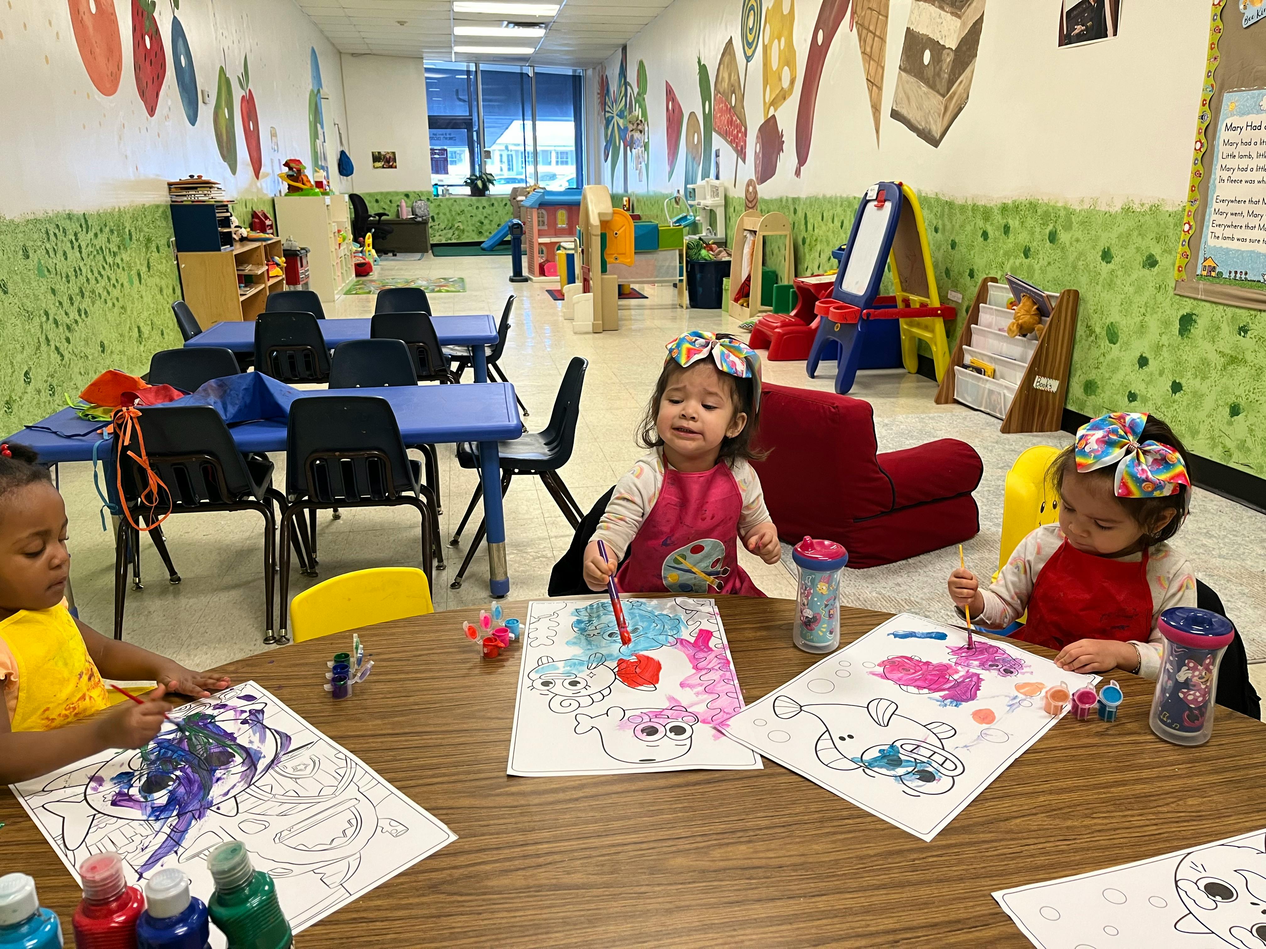 Three children painting at a table in a classroom