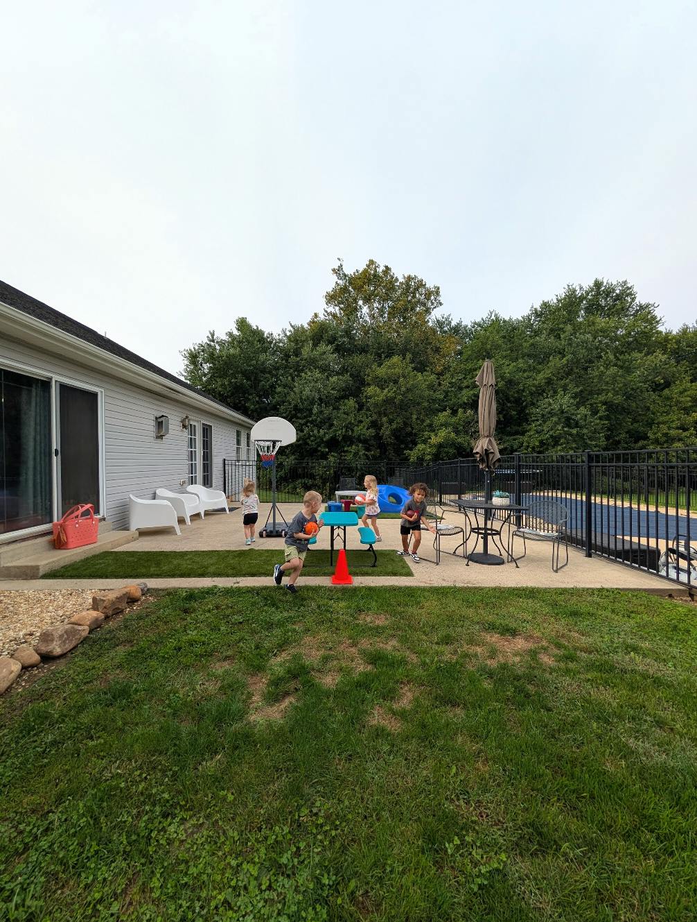 Children playing on a patio with a basketball hoop and a pool in the background