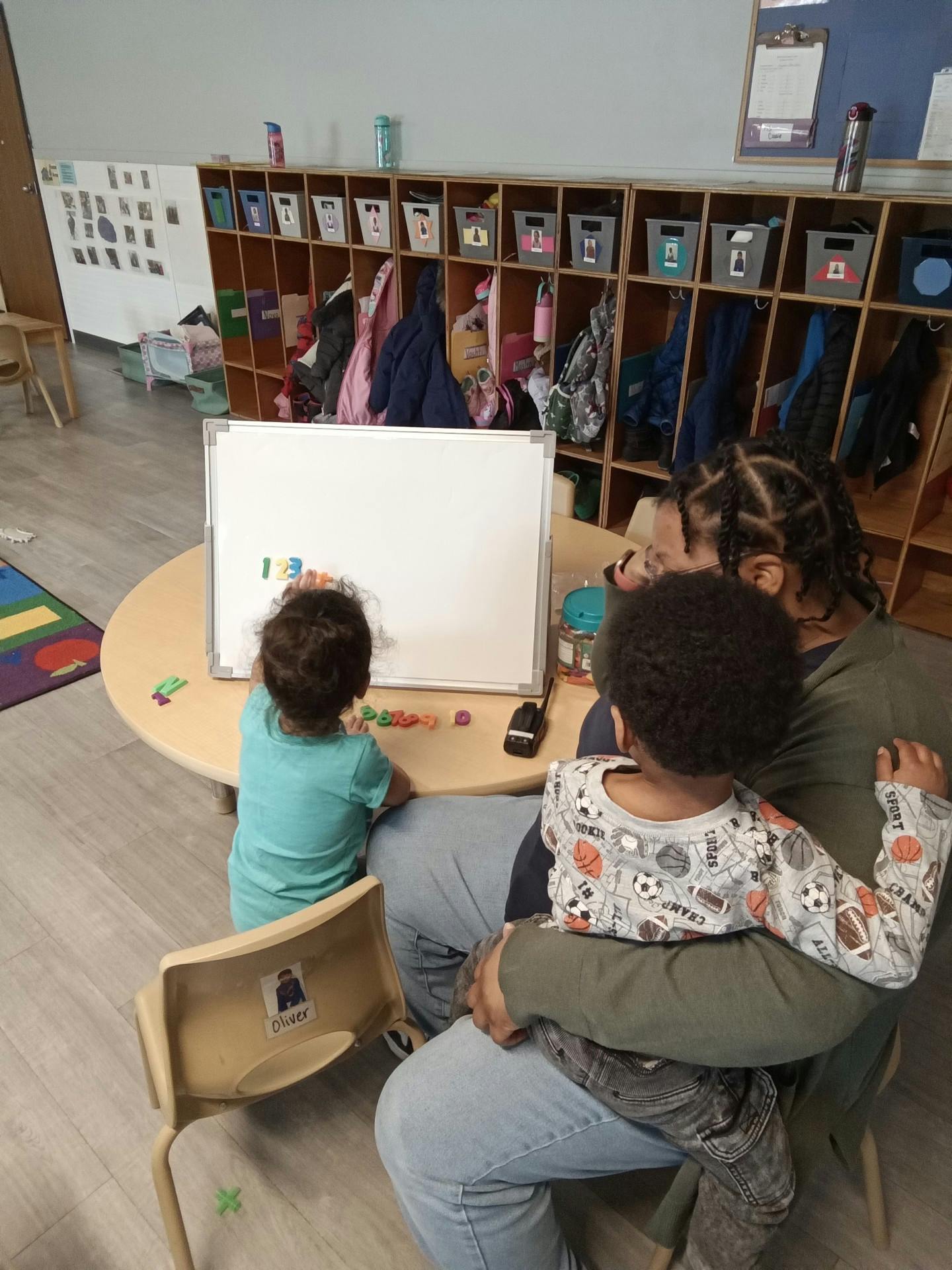 A person helping two children play with magnetic numbers on a whiteboard
