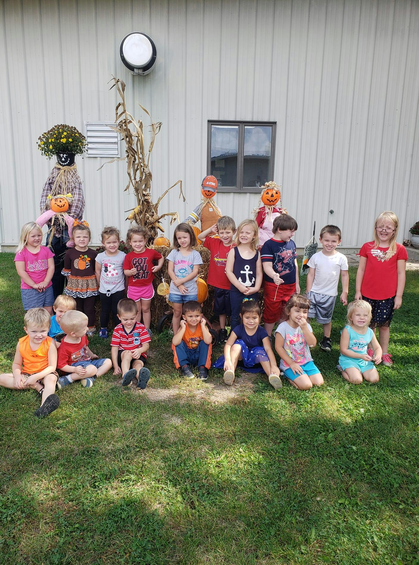 Group of children standing and sitting in front of scarecrows and corn stalks
