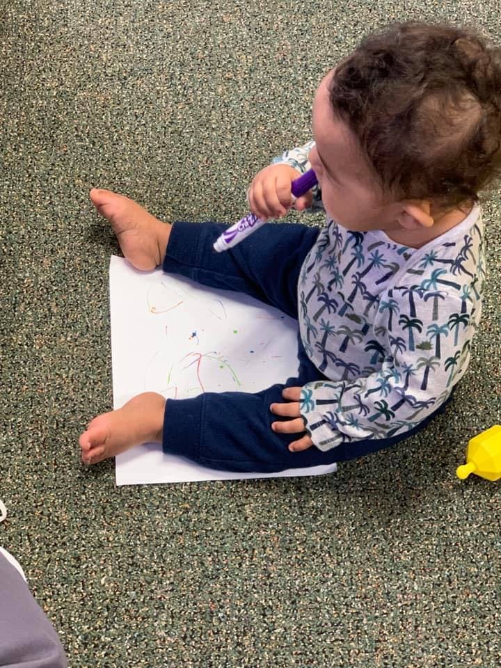 Child sitting on floor drawing on paper with a marker