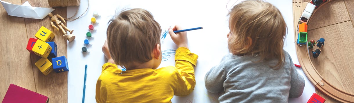 Two children drawing on a large sheet of paper