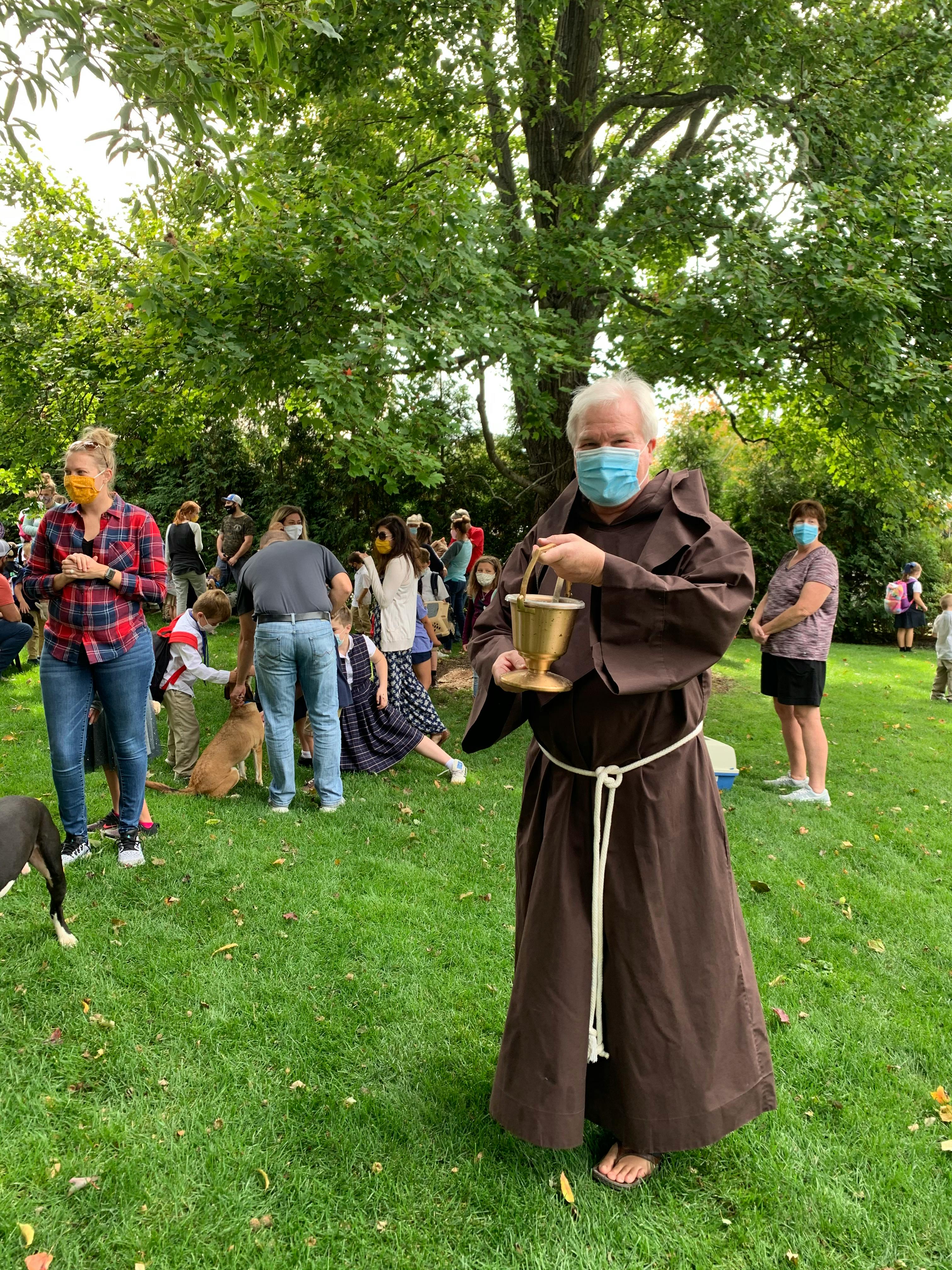 Person in a brown robe and face mask holding a golden cup outdoors