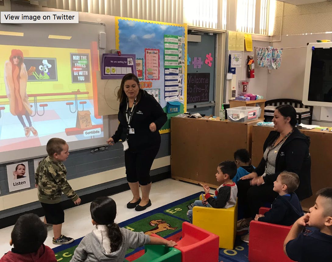 Adults and children in a classroom with a projected image