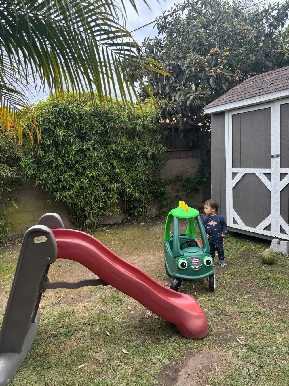 Child standing near a toy car and slide in a backyard