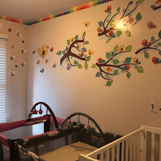 Two cribs in a room with bird and tree wall decals