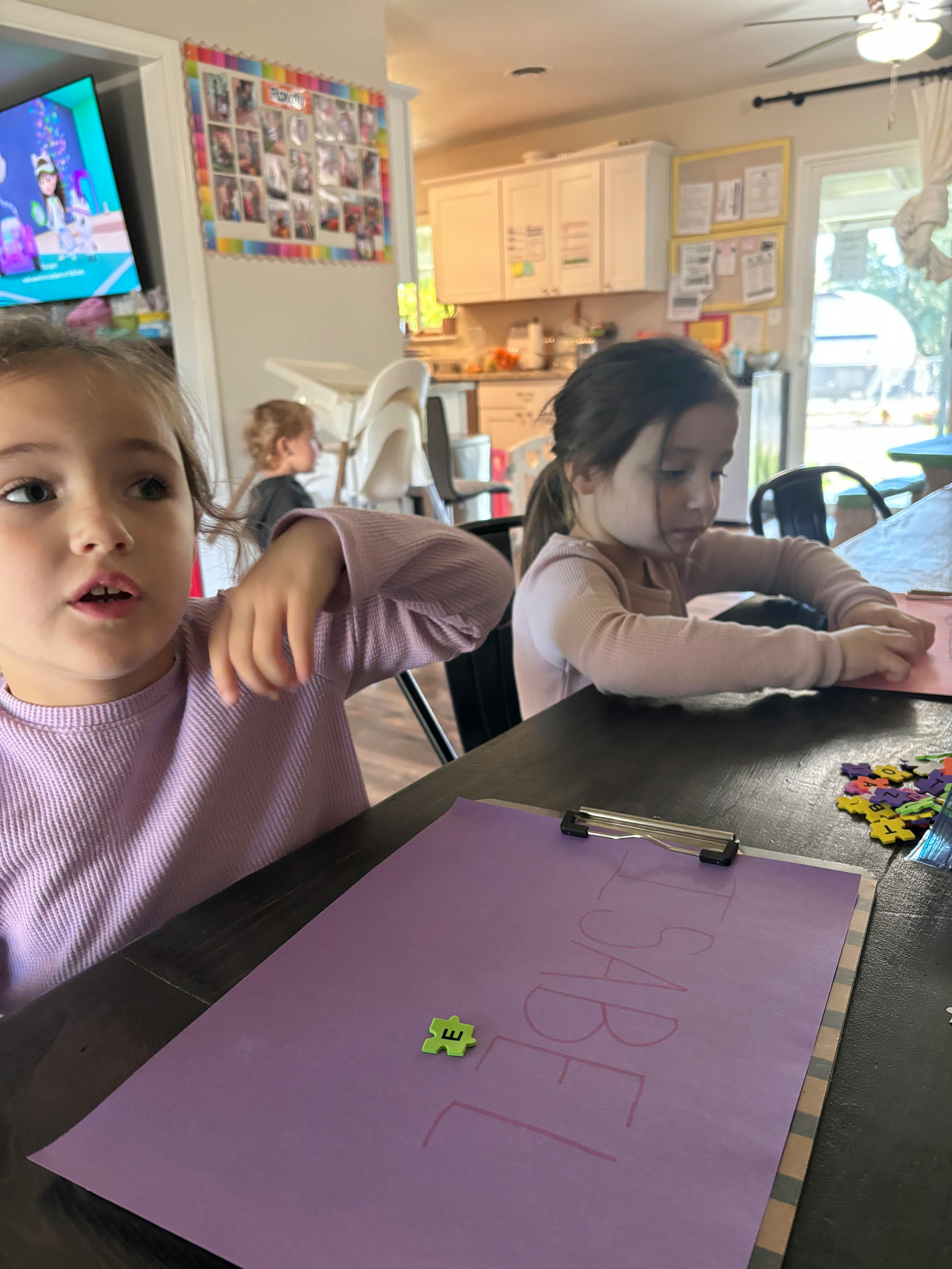 Two children at a table with one looking up and the other focused on an activity