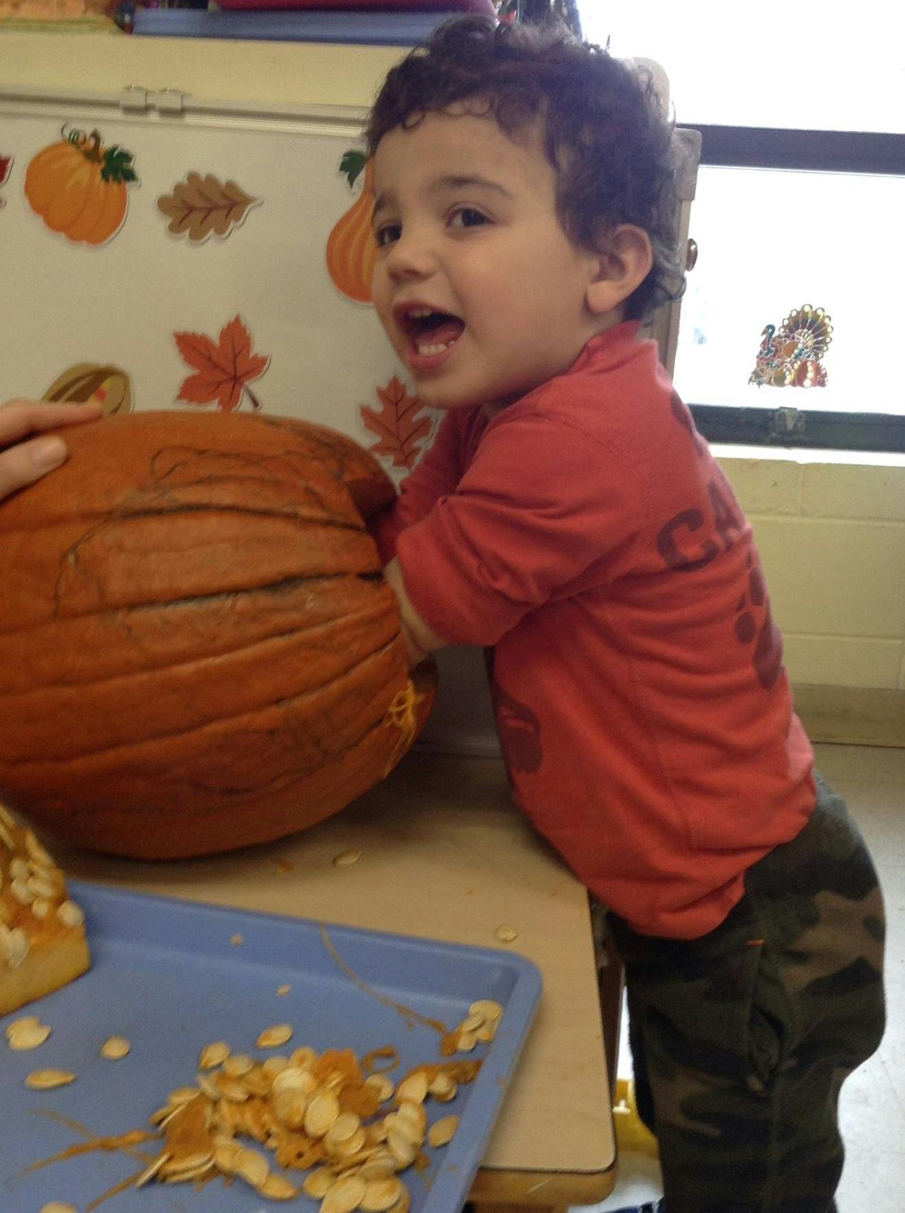 Child with open mouth next to a pumpkin with seeds on a tray