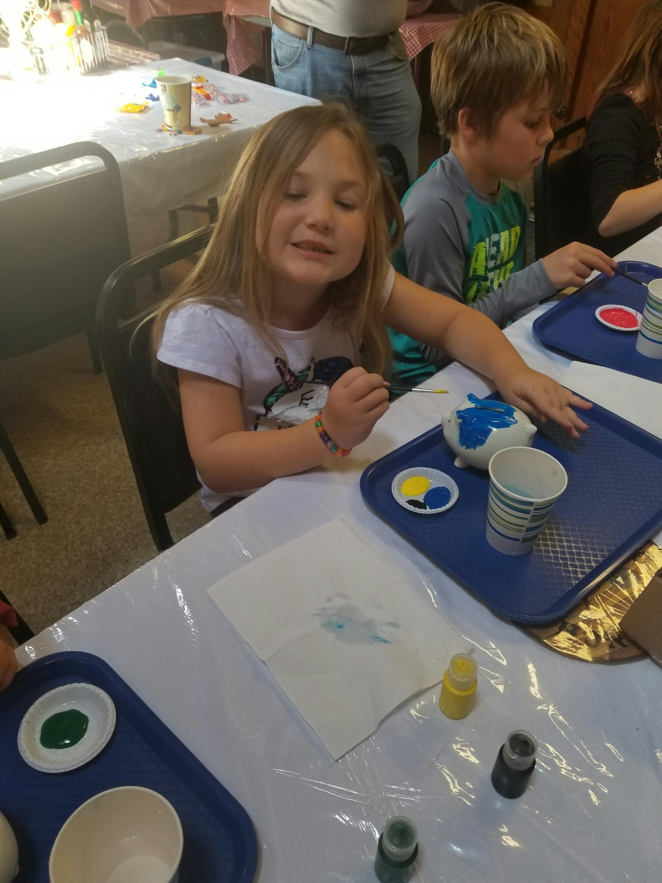 Child painting a ceramic object at a table