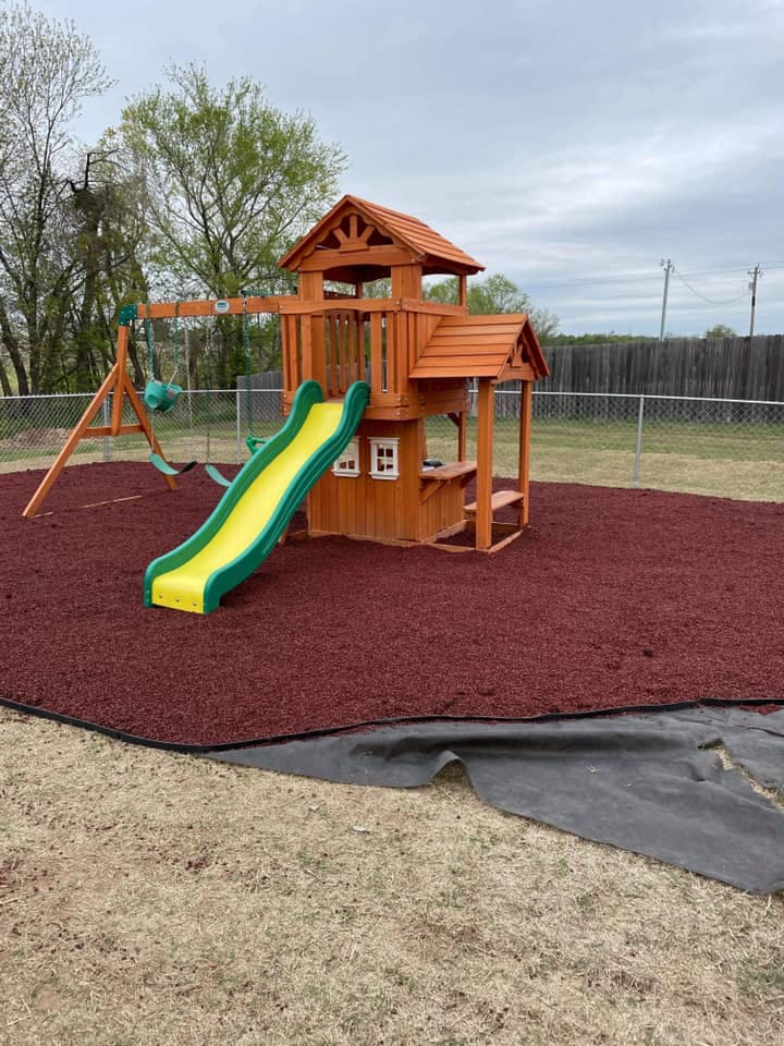 Wooden playground set with a green and yellow slide on red mulch