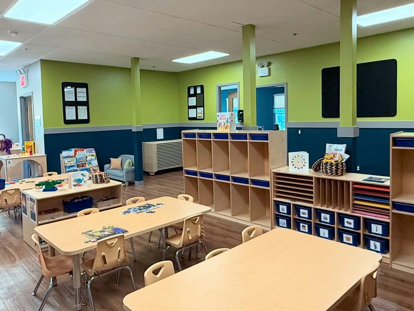 Empty classroom with small tables and chairs, storage cubbies, and green and blue walls