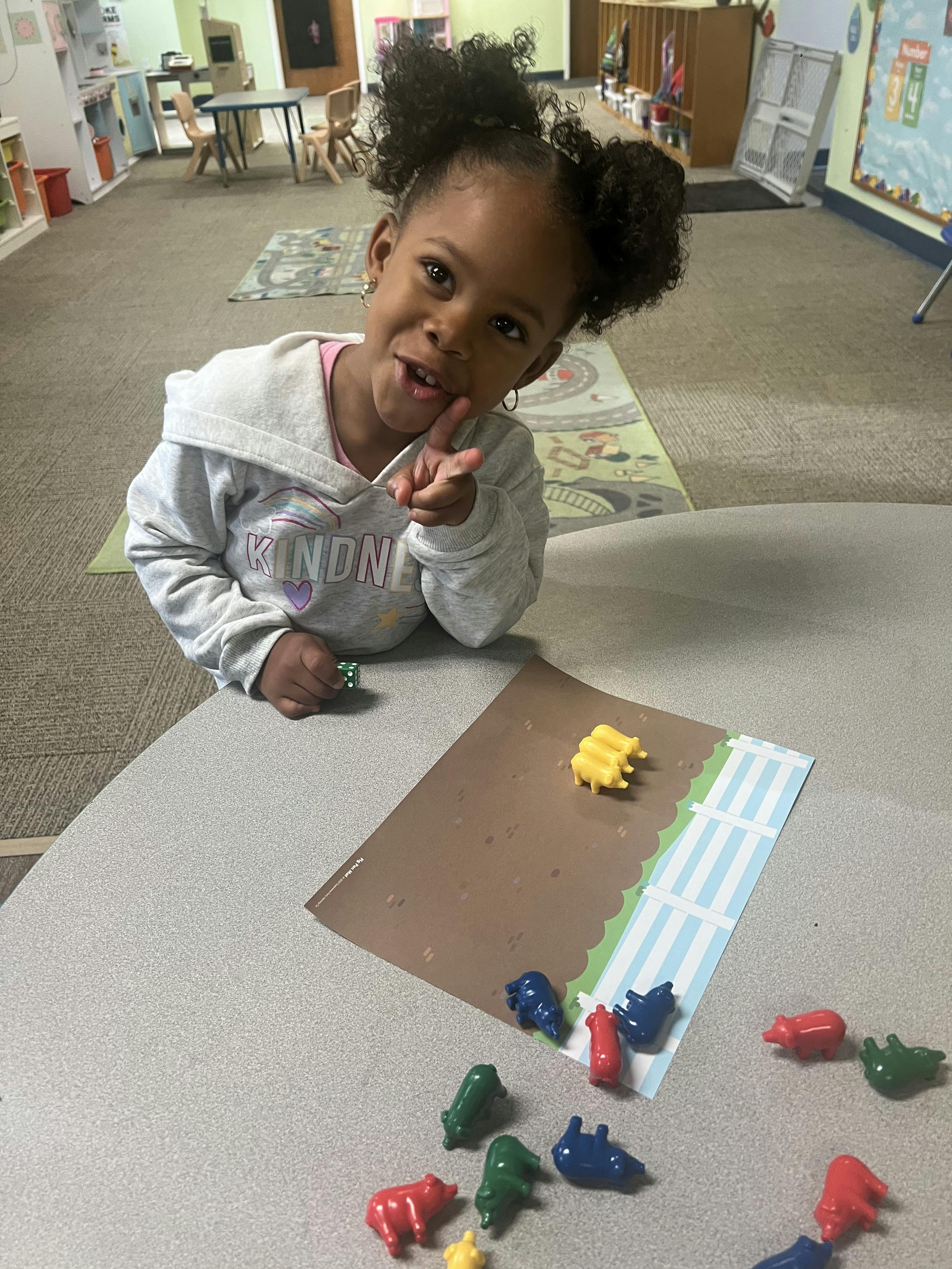 Child pointing while playing with colorful animal figures on a table