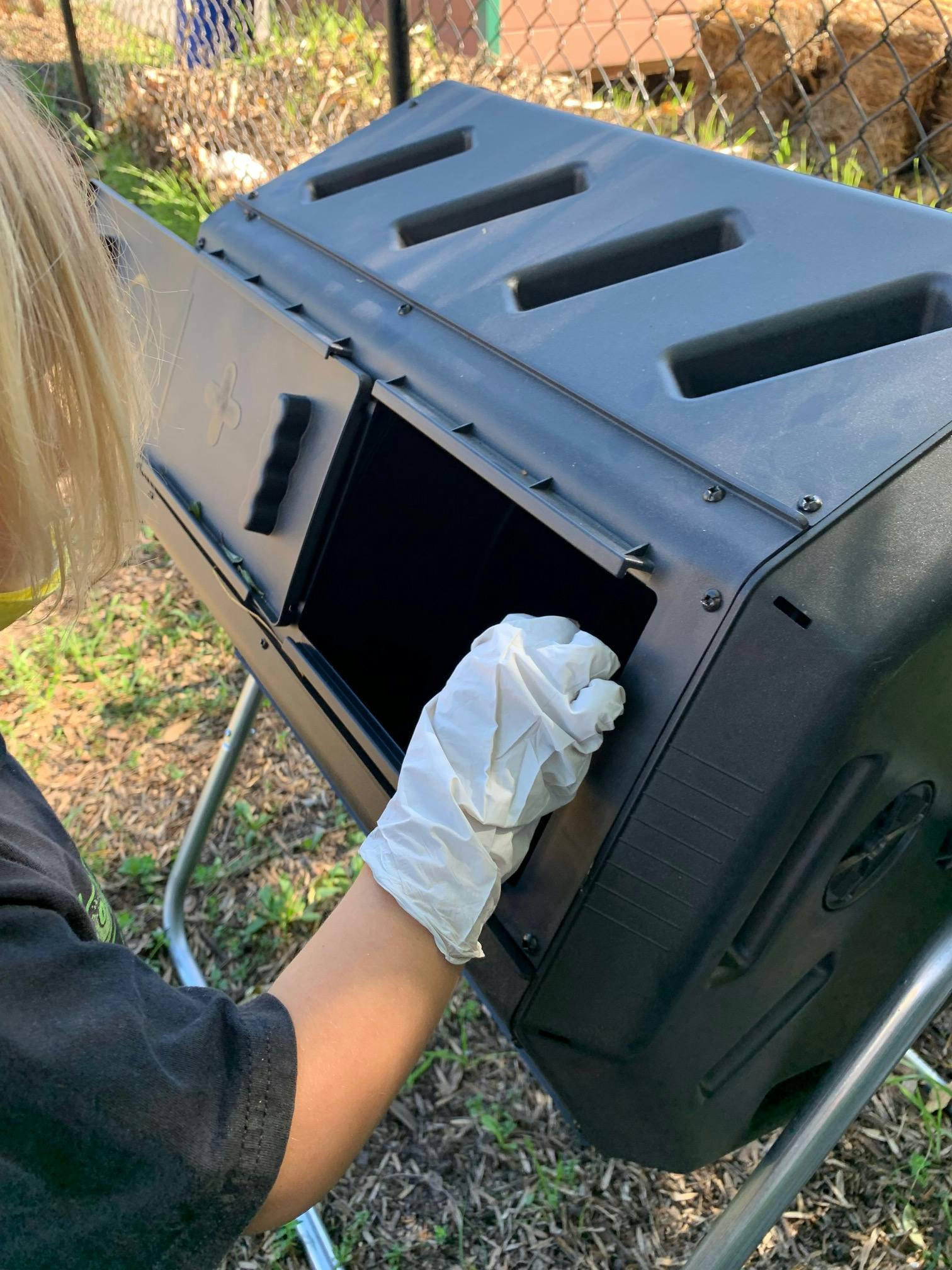 Person wearing a glove opening a black compost tumbler
