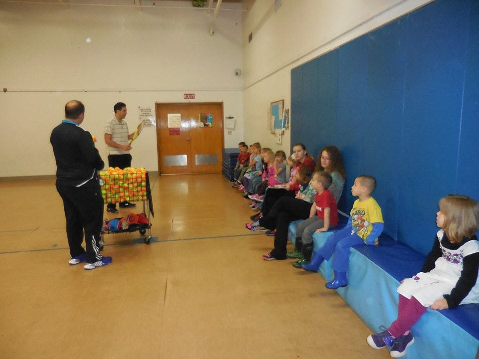 Two people standing near a cart of balls, children sitting on a bench