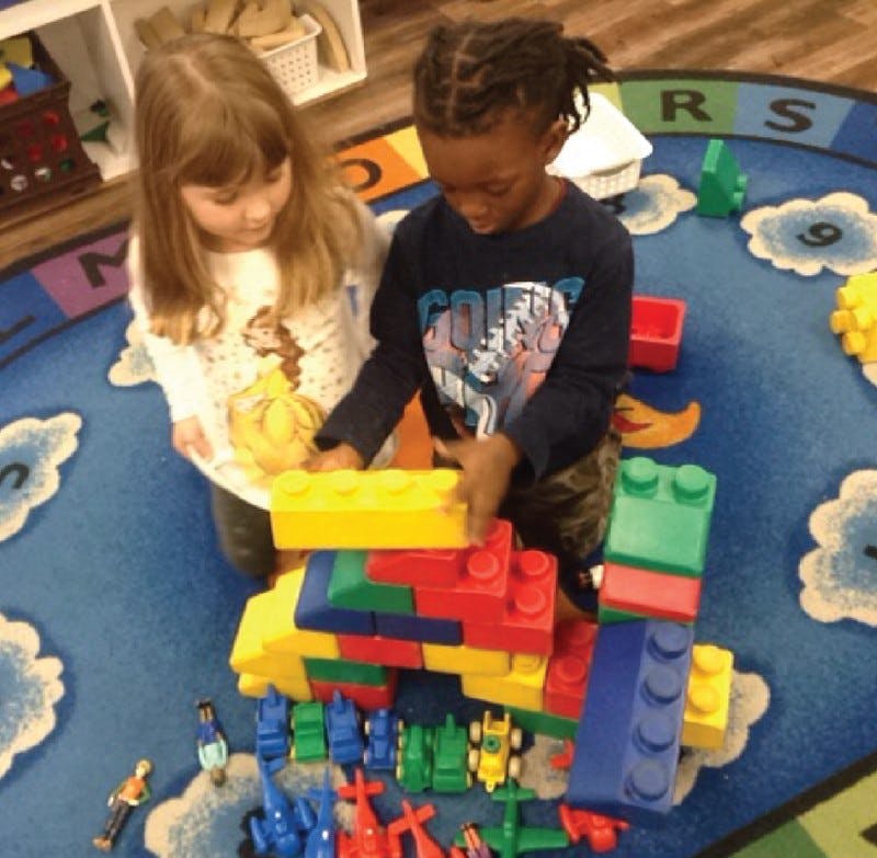 Two children playing with large colorful building blocks on a rug