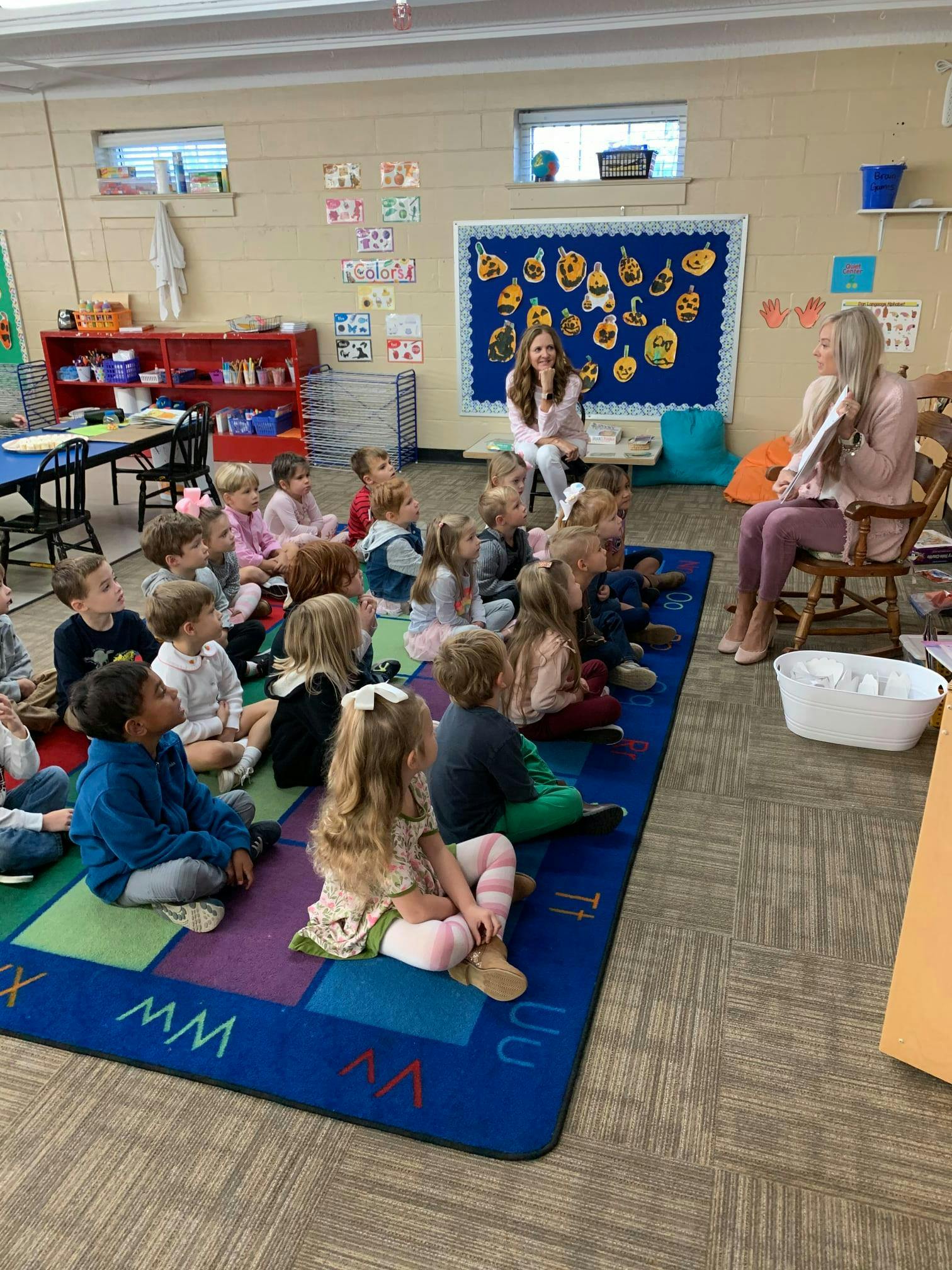 Two people reading to a group of children in a classroom