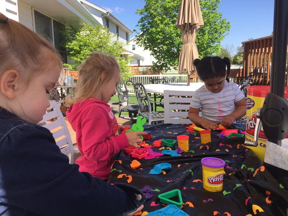 Three children playing with modeling clay at an outdoor table