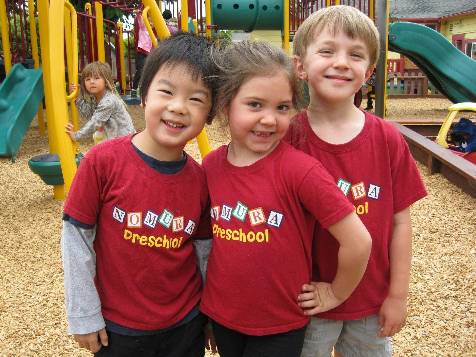 Three children in red preschool shirts on a playground