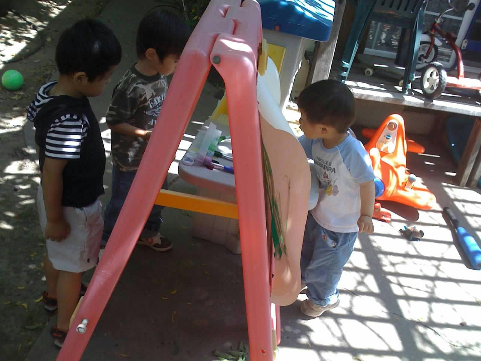 Three children playing around a pink and white easel