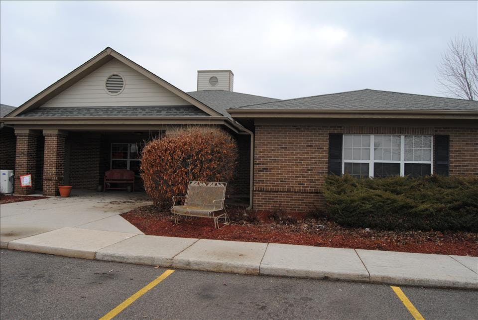 Brick building with a covered entrance, a bench, and bushes in front of it a sidewalk