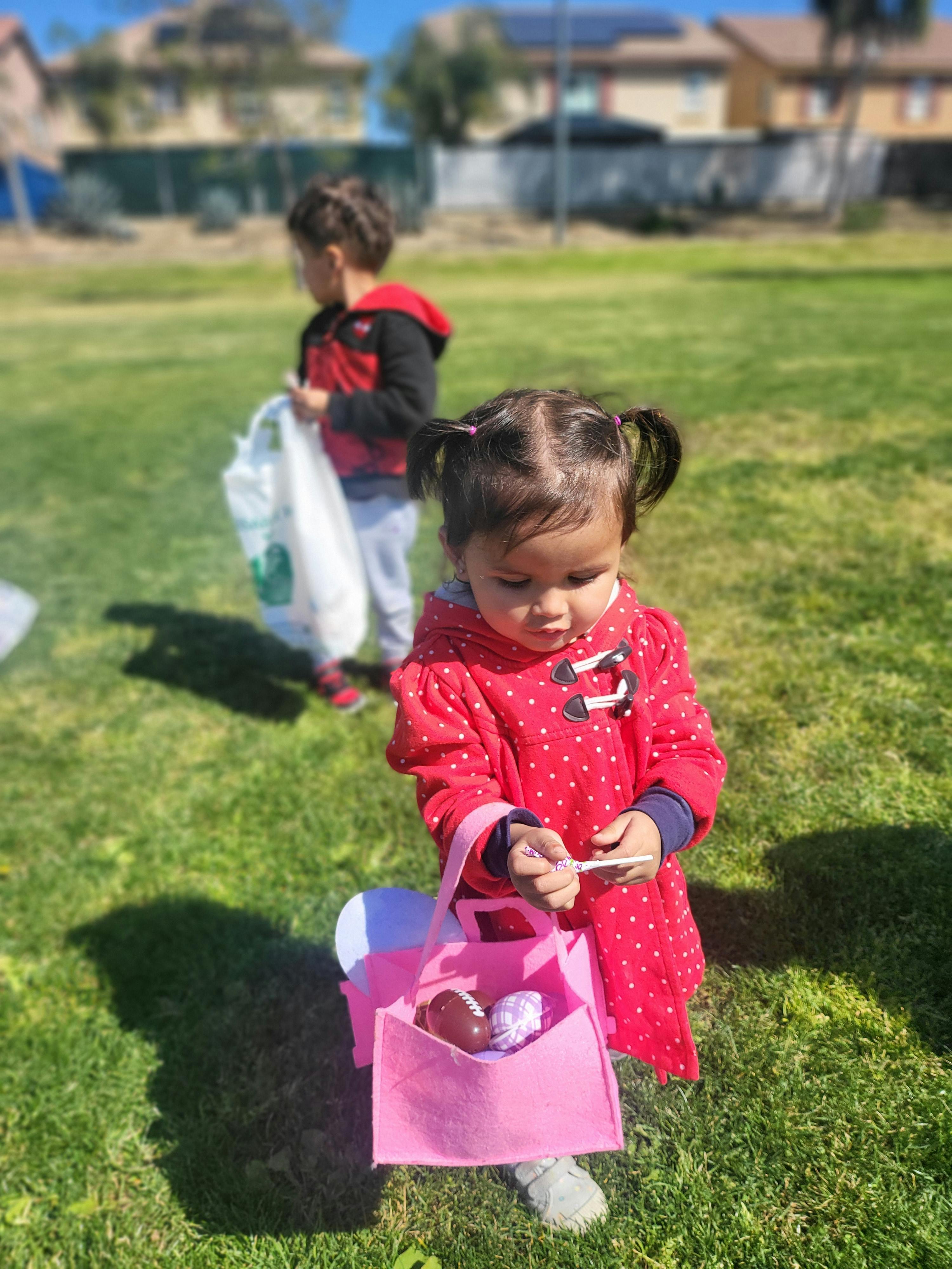 Child in red coat holding a pink bag, another child in background