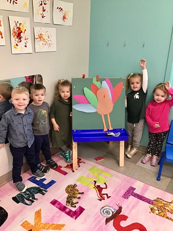 Five children standing around an easel with a turkey craft
