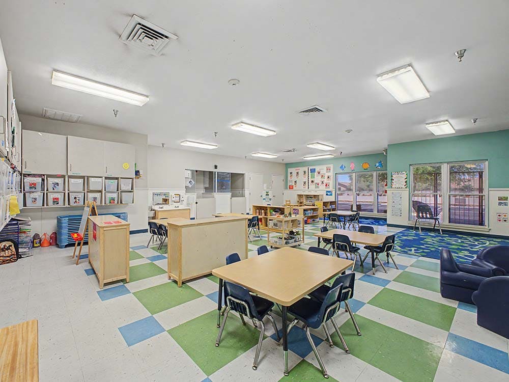 Classroom with tables, chairs, cabinets, and art on the walls