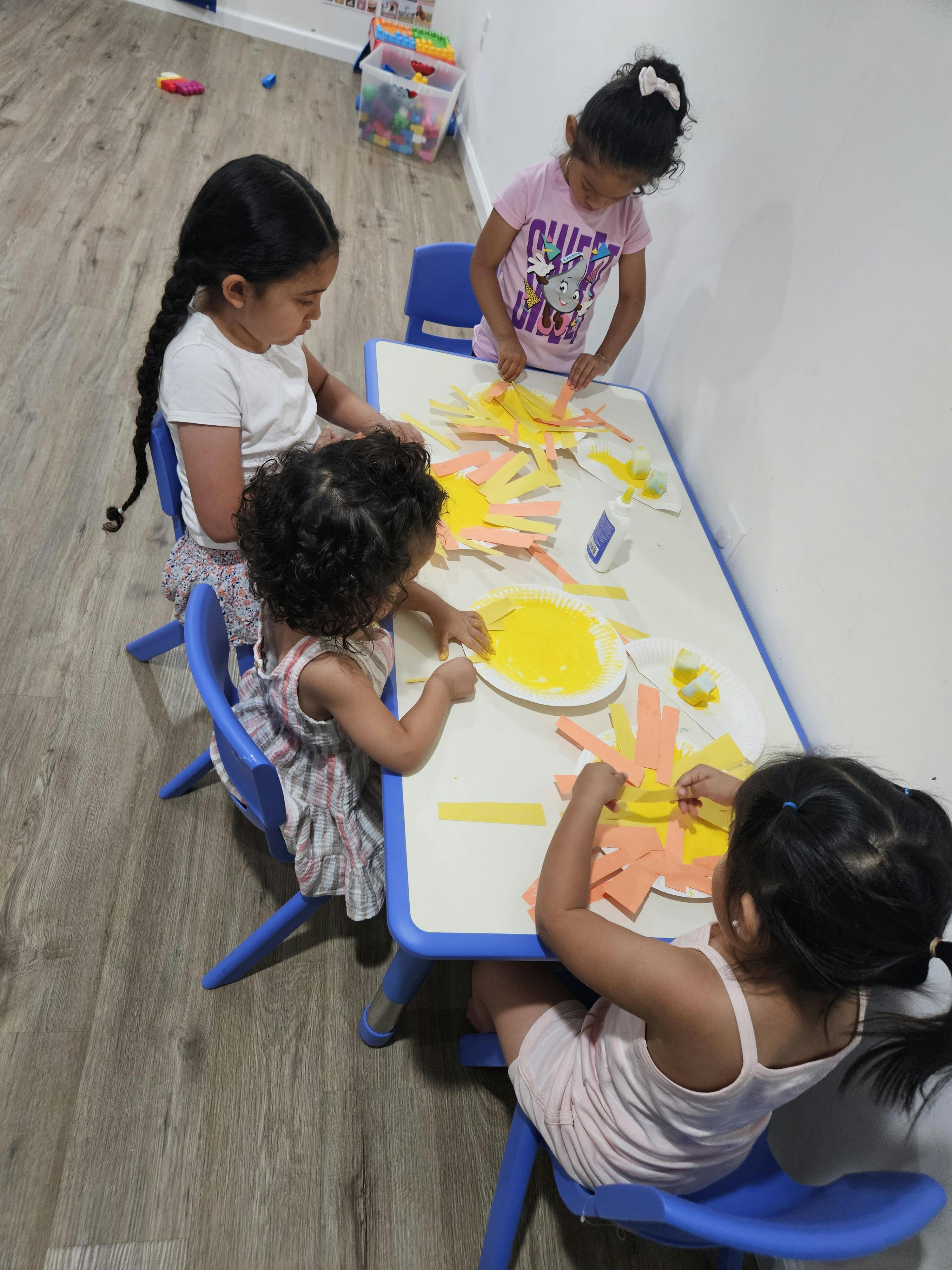 Three children sitting at a table crafting paper suns